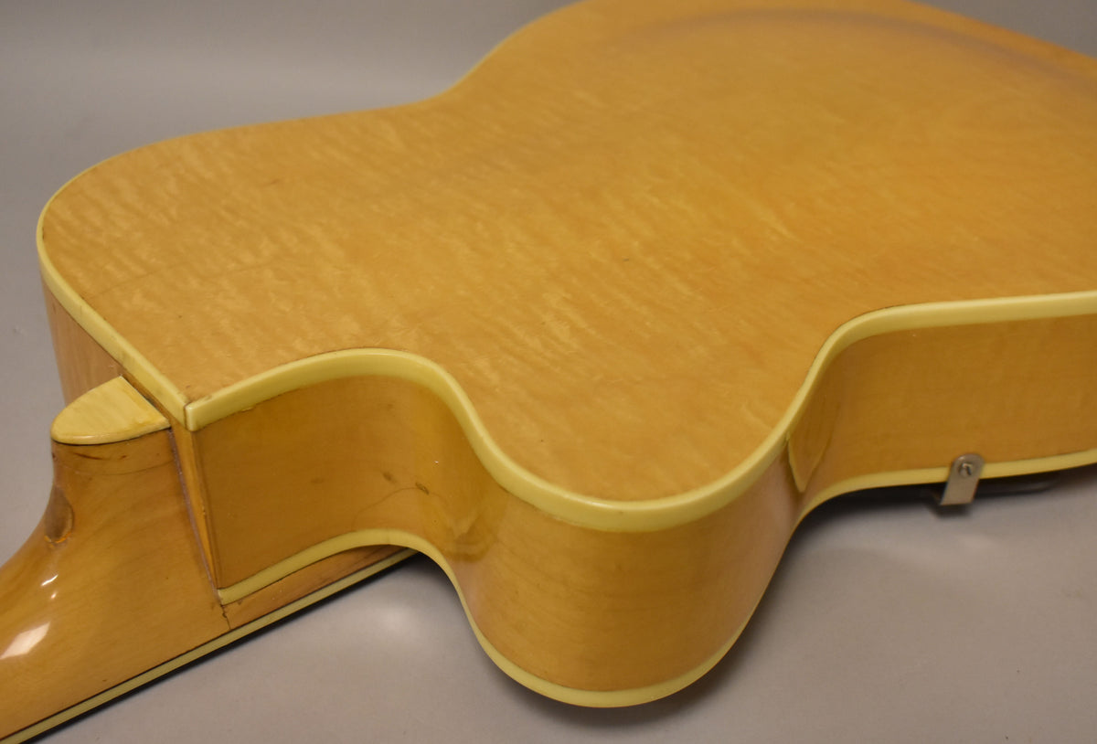 Close-up of the natural finish archtop guitar's lower body, showing the cutaway, neck heel, and some finish checking on the side.