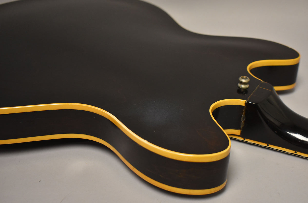 Close-up of the guitar's lower bout and neck heel, showing dark walnut finish, cream binding, and a chipped neck joint.
