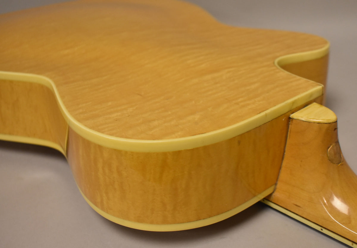 Upper bout and cutaway of a natural finish archtop guitar, showing flame maple grain, cream binding, and some finish wear on the neck heel.