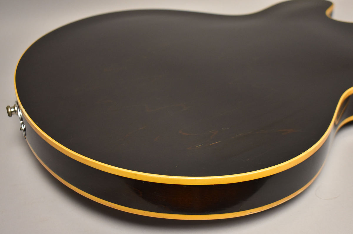 The guitar's dark walnut back and side are visible, with cream binding and a chrome strap button, showing light surface wear.