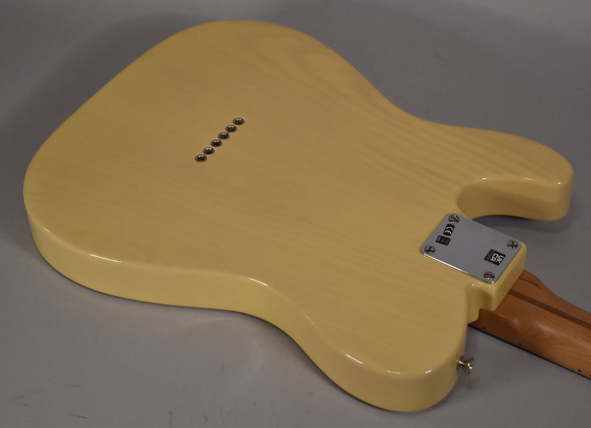 The back of a blonde Telecaster body, showing the string-through-body ferrules, neck plate, and strap button.