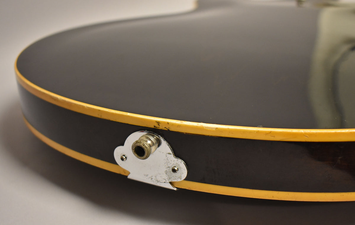 Close-up of the guitar's lower bout, showing the dark walnut finish, cream binding, and a worn chrome output jack plate.