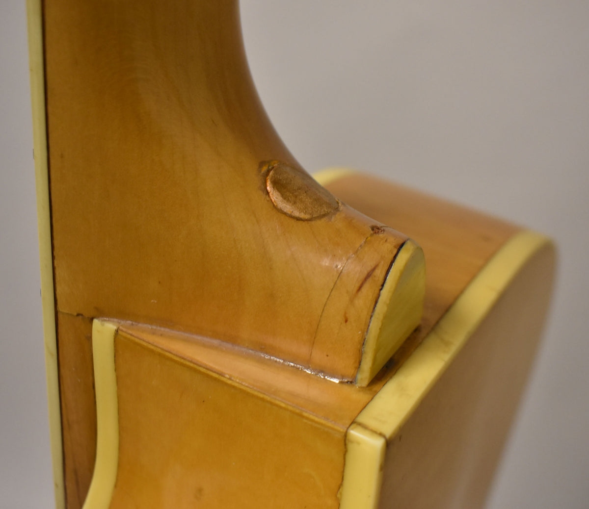 Close-up of the guitar's natural finish neck heel, showing binding, a circular strap button, and visible finish wear and checking.