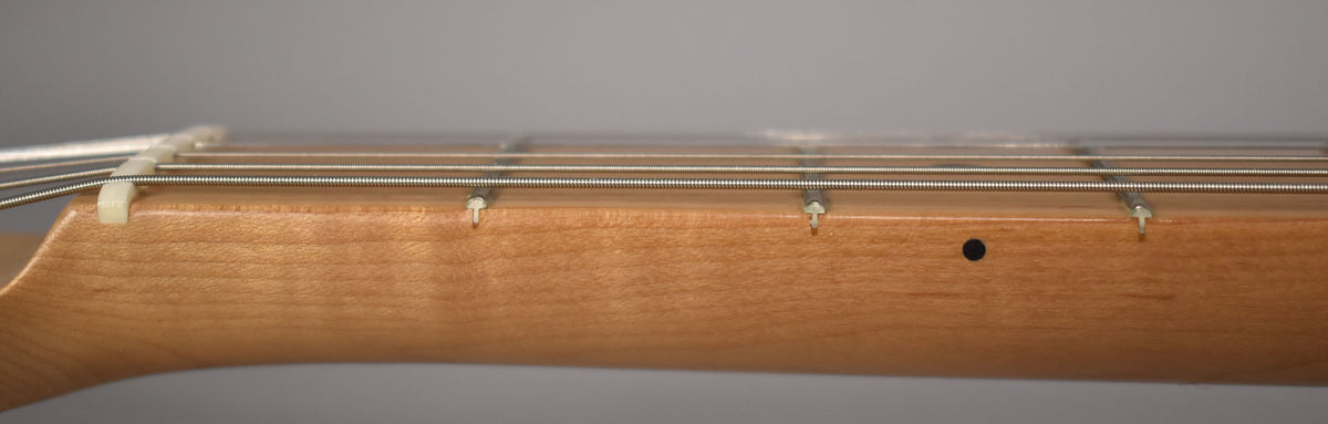Close-up of the light brown maple neck and fretboard, showing the nut, strings, and a black side dot marker.