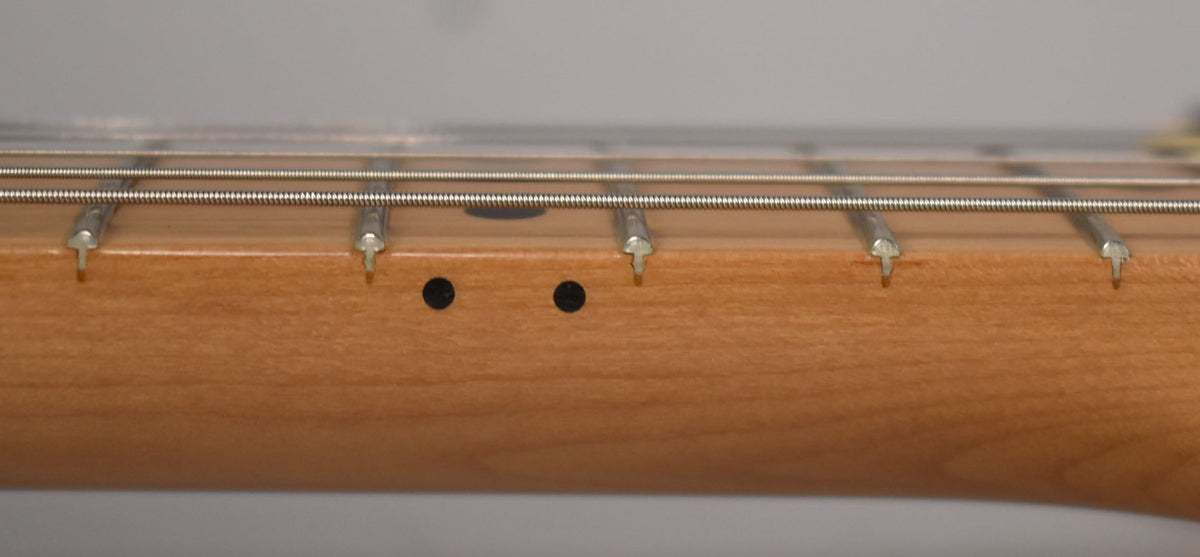 Close-up of the light brown maple neck and fretboard, showing four frets, three strings, and two black side dot markers.