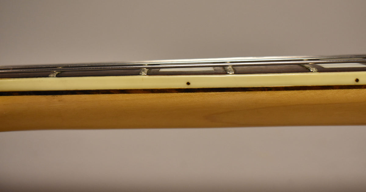 The guitar neck's side is visible, showing a light wood finish, cream binding, and dark fretboard with small dot markers and strings.