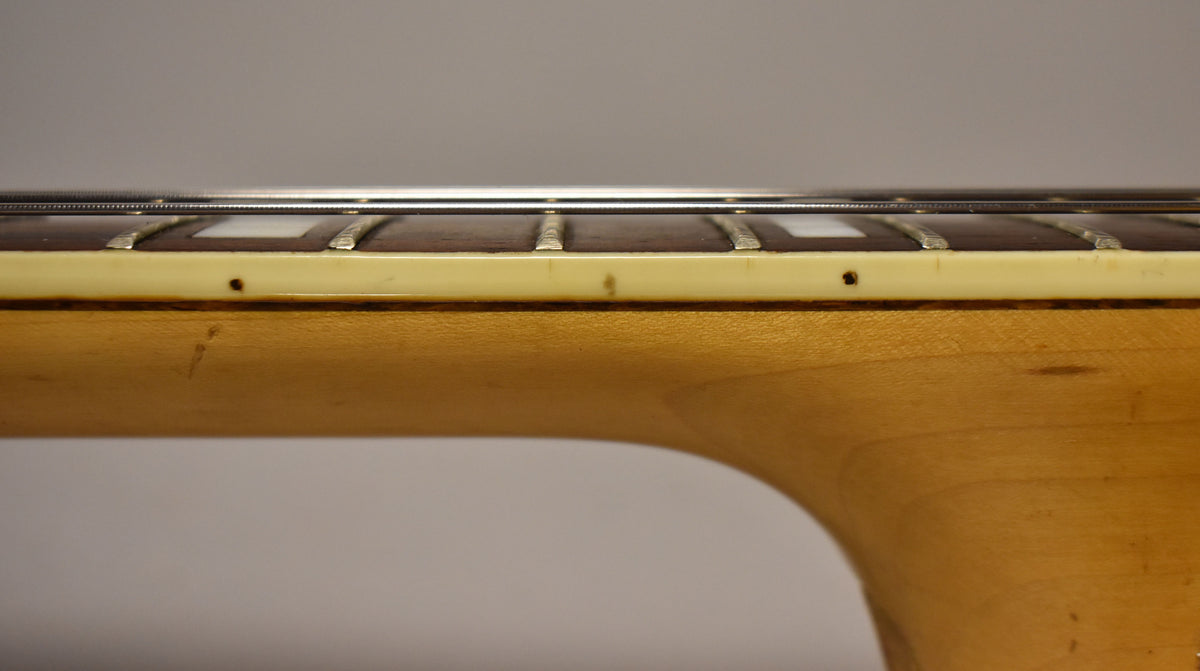 Close-up of the guitar's natural finish neck and dark fretboard with rectangular inlays, showing some wear and small dark spots.