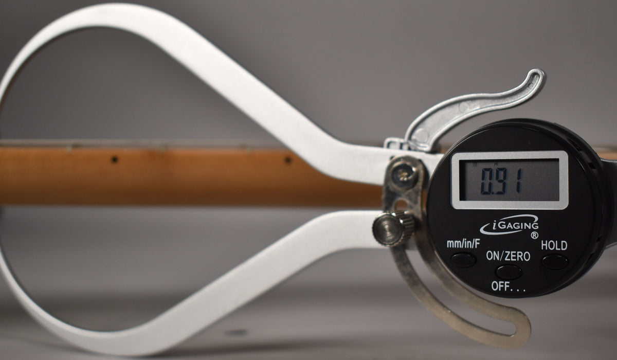A digital caliper measures the guitar's roasted maple neck, displaying "0.91" on its screen.