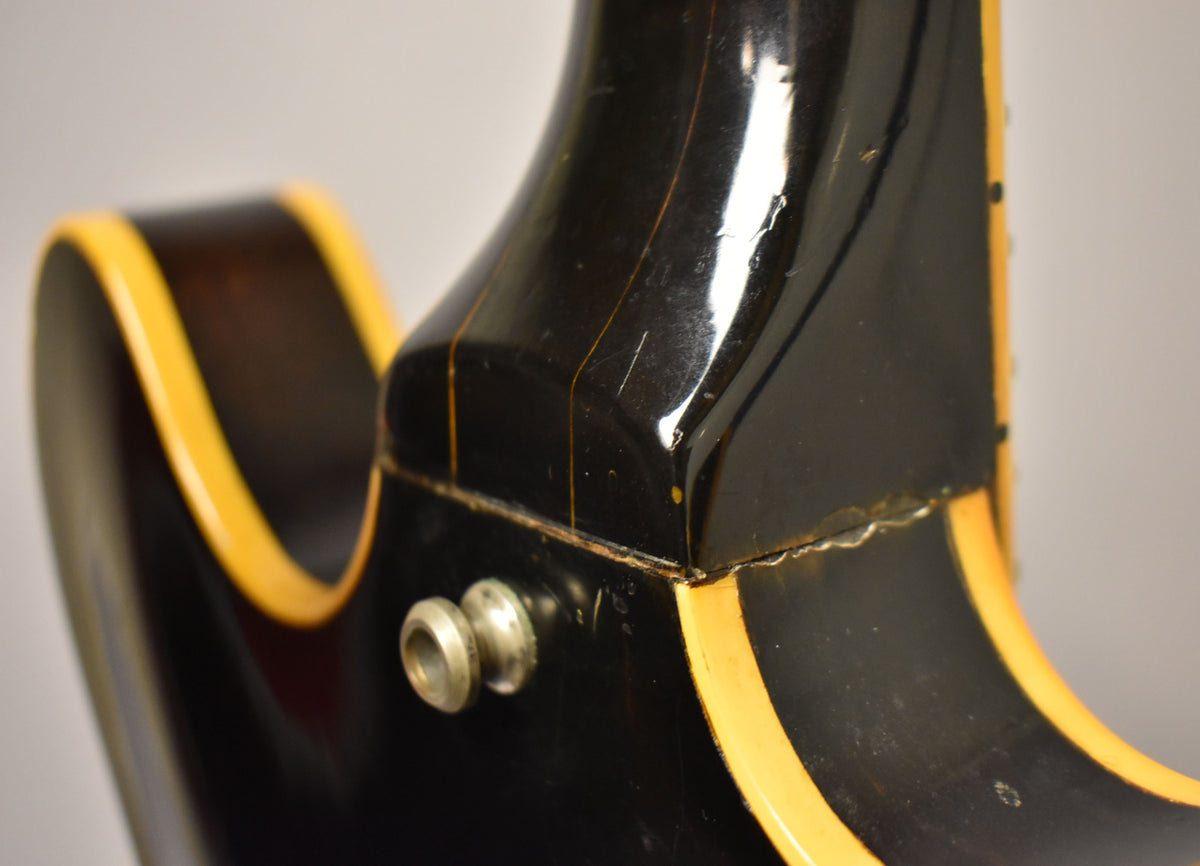 Close-up of the guitar's dark walnut neck heel, showing finish checking, wear, and a chrome strap button.