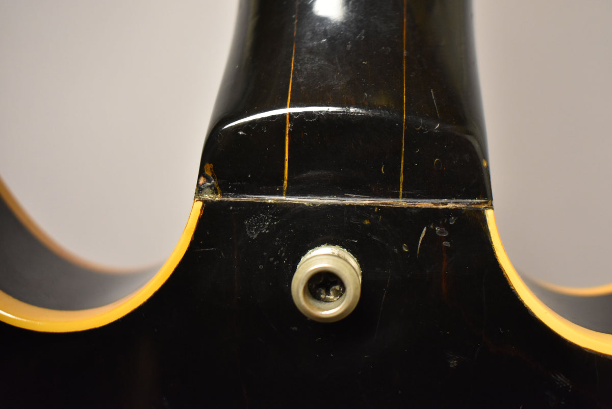 Close-up of the guitar's black neck heel and body, showing finish checking, wear, and the output jack.