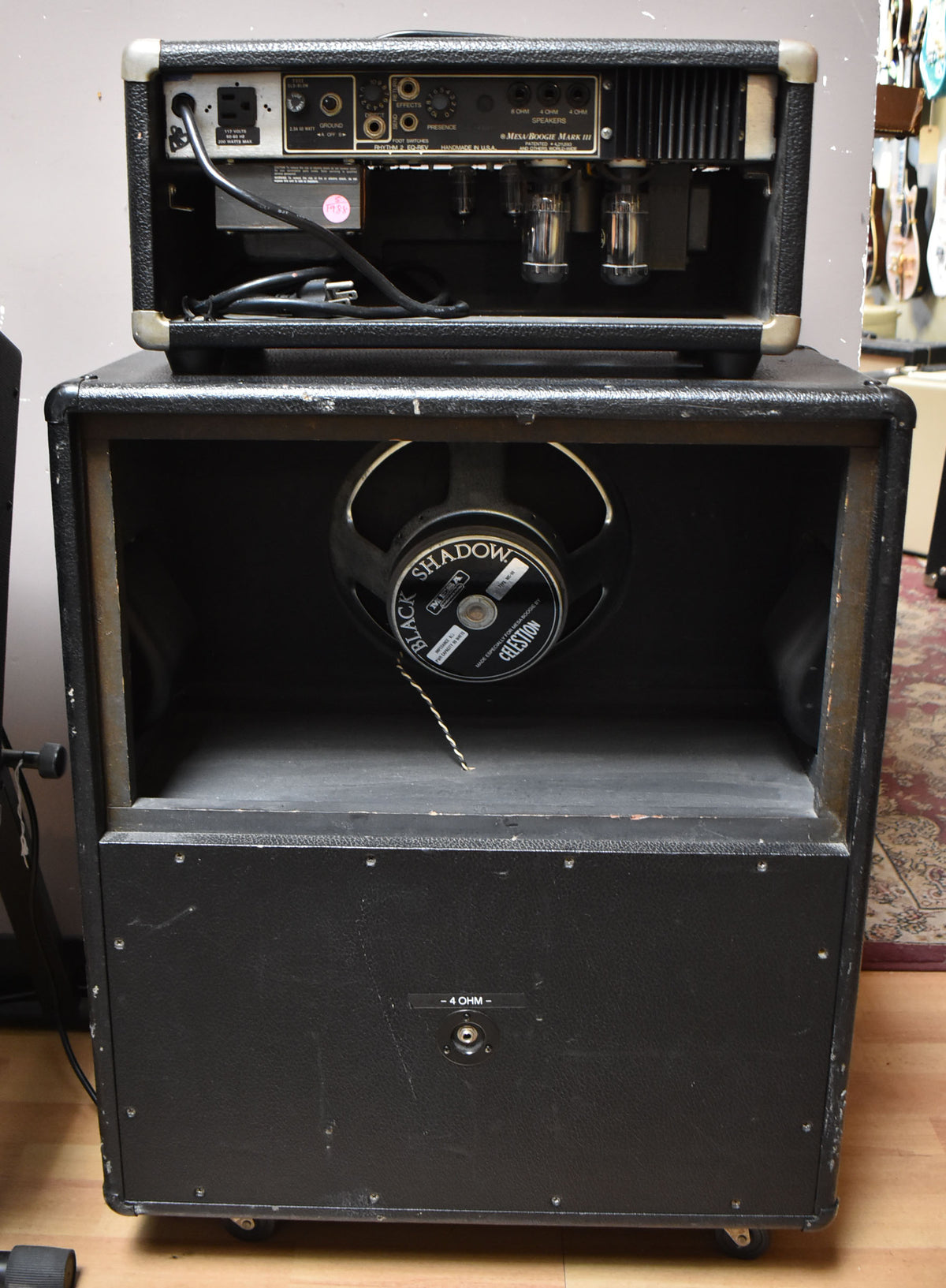 The black amp head's rear panel with exposed tubes sits atop the matching cabinet, revealing one Celestion speaker.