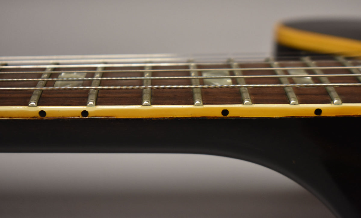 Close-up of the guitar's dark fretboard and frets, showing side dot markers and cream binding with some wear.