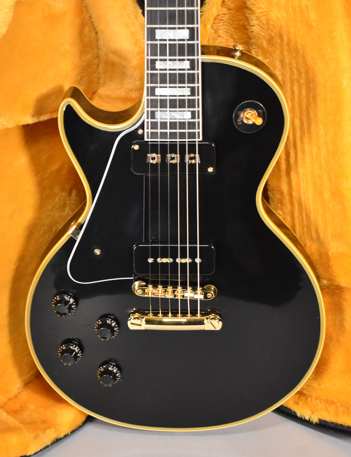 Full-frame view of a glossy black Les Paul with gold hardware, two P90 pickups, and four black control knobs.