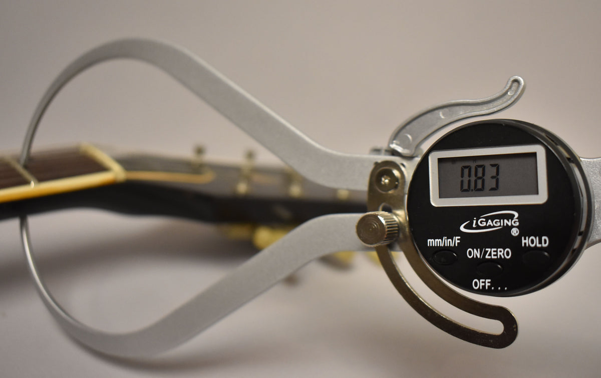A digital caliper measures the guitar's nut height at 0.83mm, with the dark headstock and fretboard visible in the background.