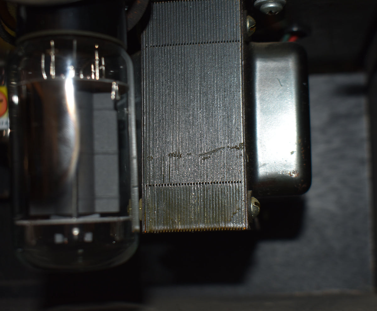 Close-up of internal components, showing a large vacuum tube next to a ribbed transformer with visible wear and some corrosion.