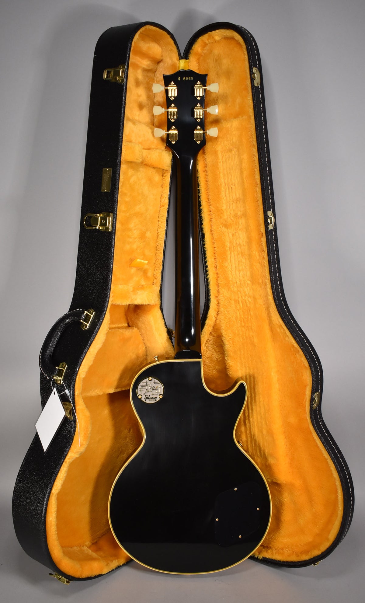 The guitar's glossy black back and headstock with gold tuners are visible, resting in an open black case with orange plush lining.