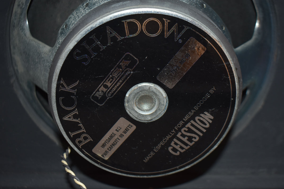 Close-up of a black speaker cone with a silver frame, showing the central dust cap and a black label with white text.