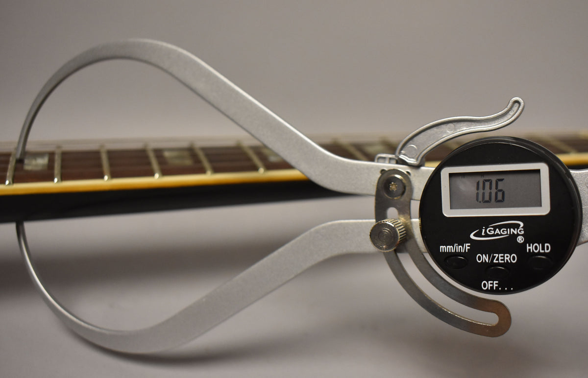 A digital caliper measures the guitar's neck thickness at 1.06 inches, showing the dark fretboard and binding.