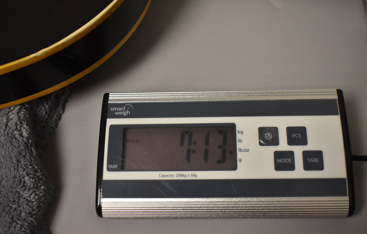 A digital scale displays "7.13" lbs, with the guitar's black body and yellow binding visible in the upper left.