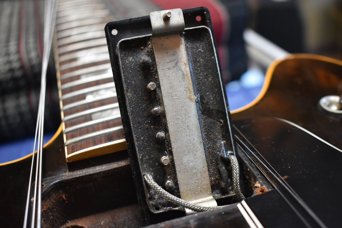Close-up of a dusty, tarnished black humbucker pickup with exposed wiring, showing wear on the walnut body and fretboard.
