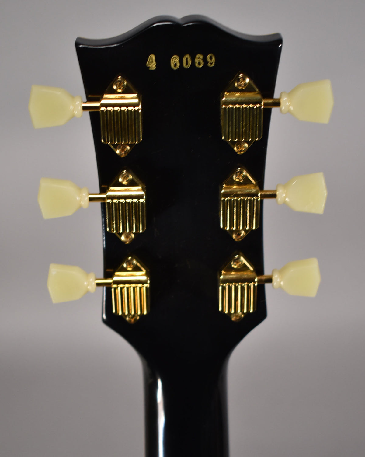 Rear view of the glossy black headstock and neck, showing six gold tuners with cream plastic buttons.
