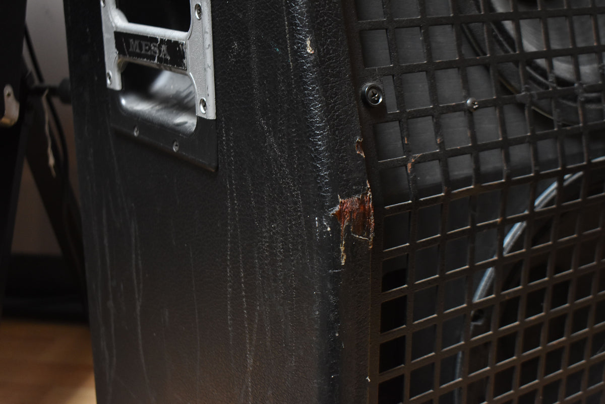 Close-up of the black tolex cabinet's side, showing a silver handle, scuffs, and a large tear exposing wood near the metal grille.