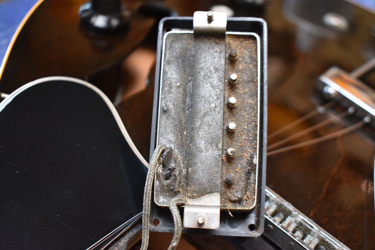 Close-up of a rusty, tarnished humbucker pickup with exposed wiring, showing heavy wear and grime.