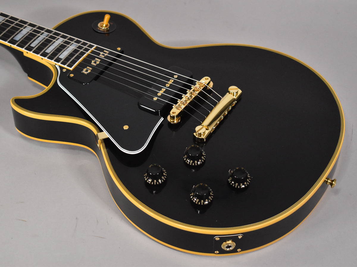 Close-up of a black Les Paul's body, showing gold hardware, black pickguard, four black control knobs, and cream binding.