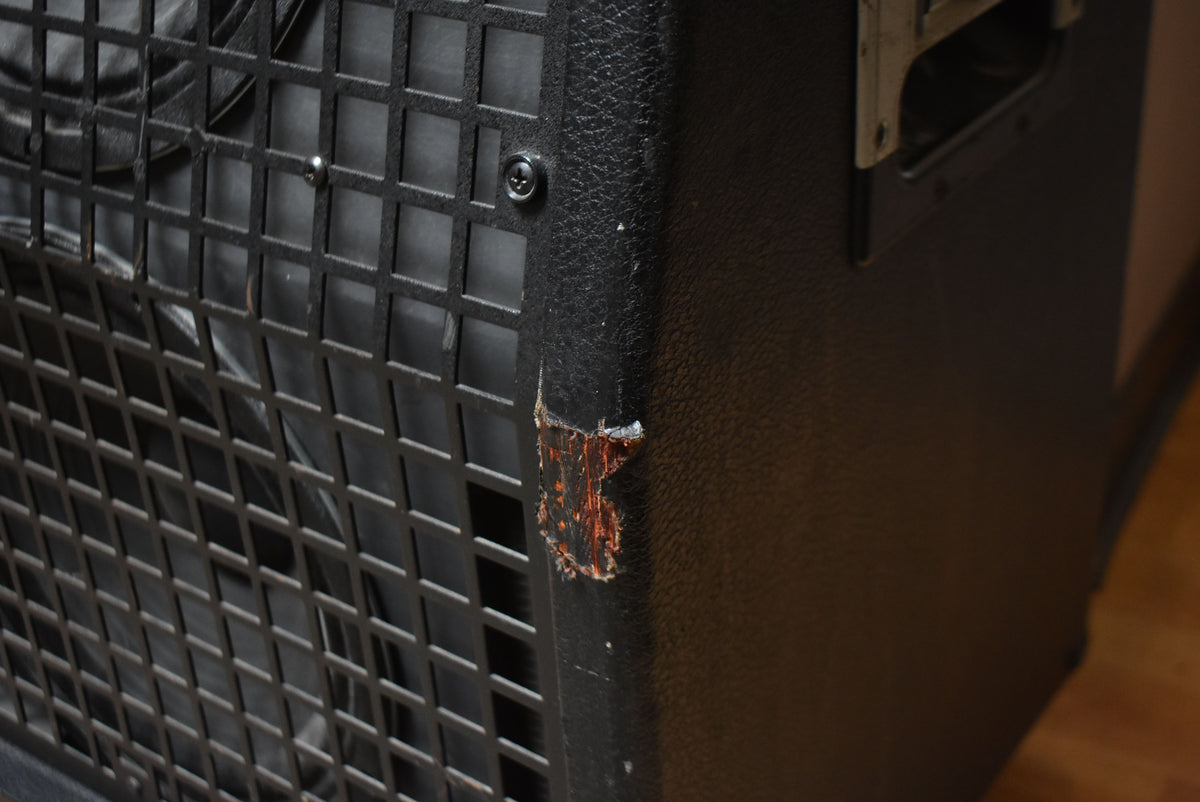 Close-up of the black tolex cabinet's corner, revealing a large tear exposing the reddish wood underneath.