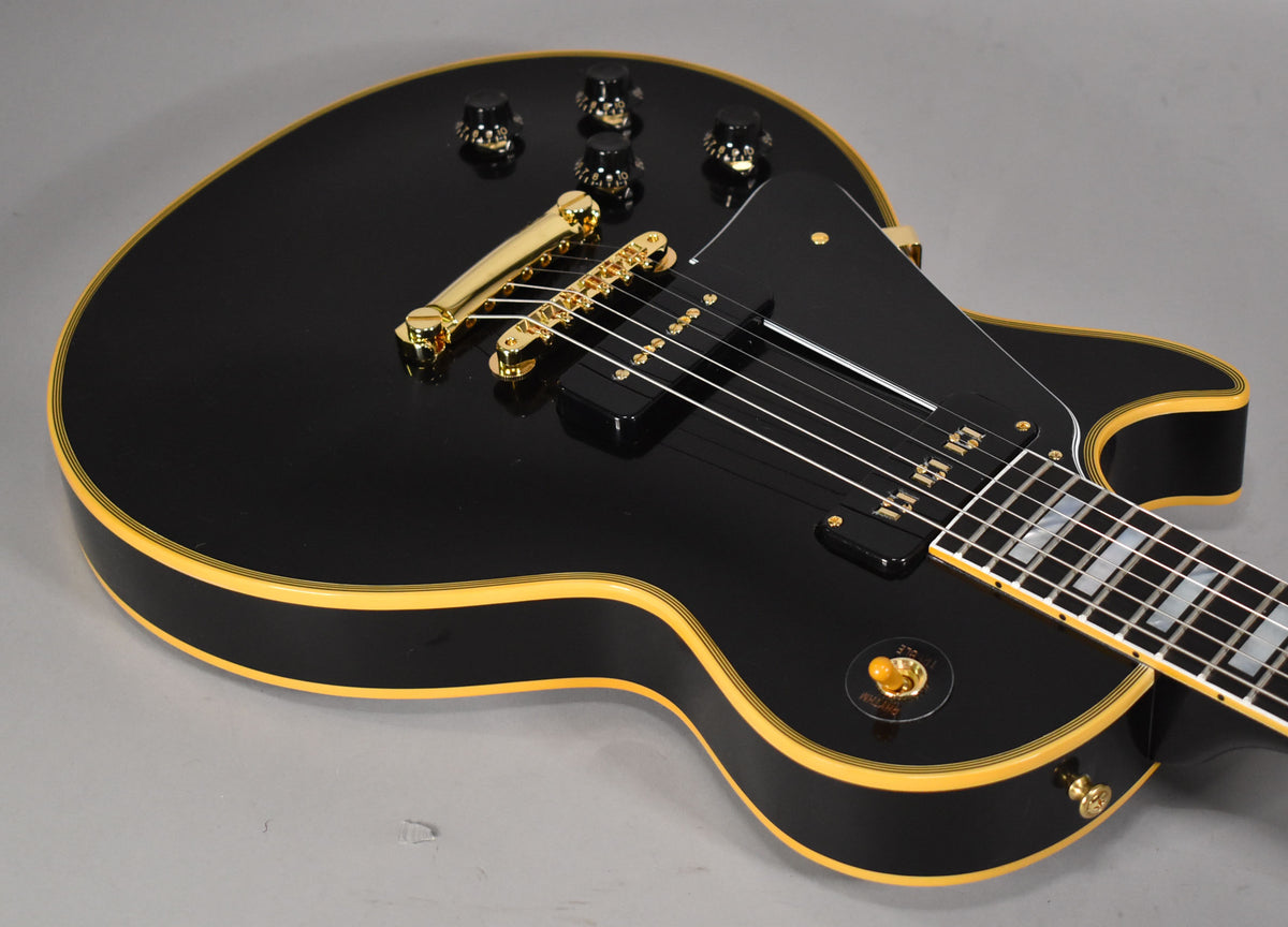 The glossy black guitar body, with cream binding, shows gold hardware and a black pickguard, angled from the lower bout.