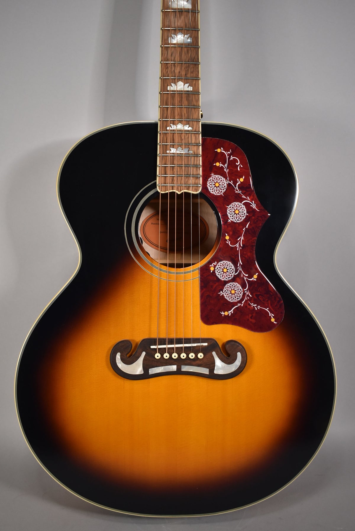 Full-frame, front view of a sunburst acoustic guitar with a decorative pickguard and ornate fretboard inlays.