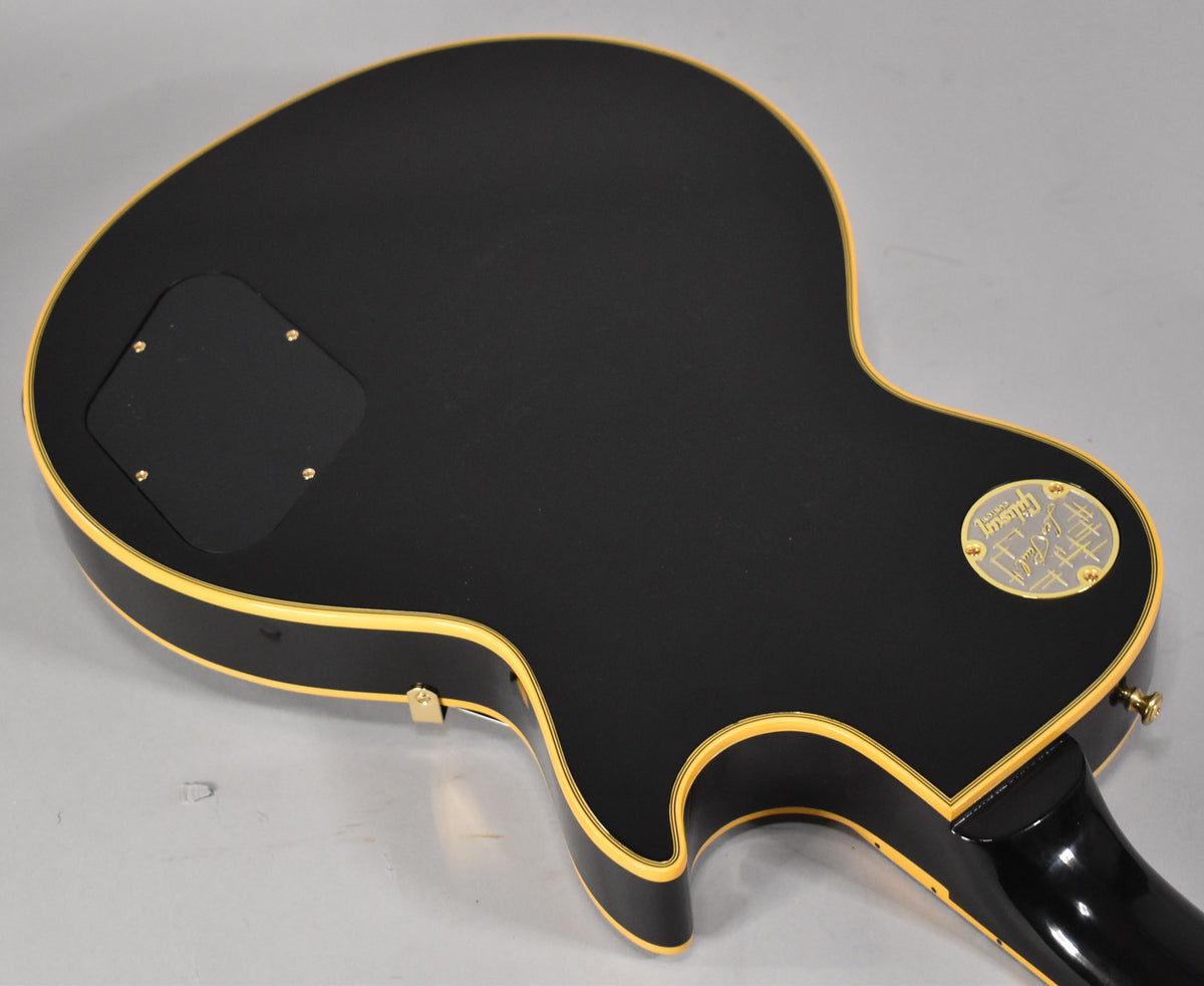 The back of an ebony Les Paul with cream binding, showing the control cavity cover and a gold medallion.