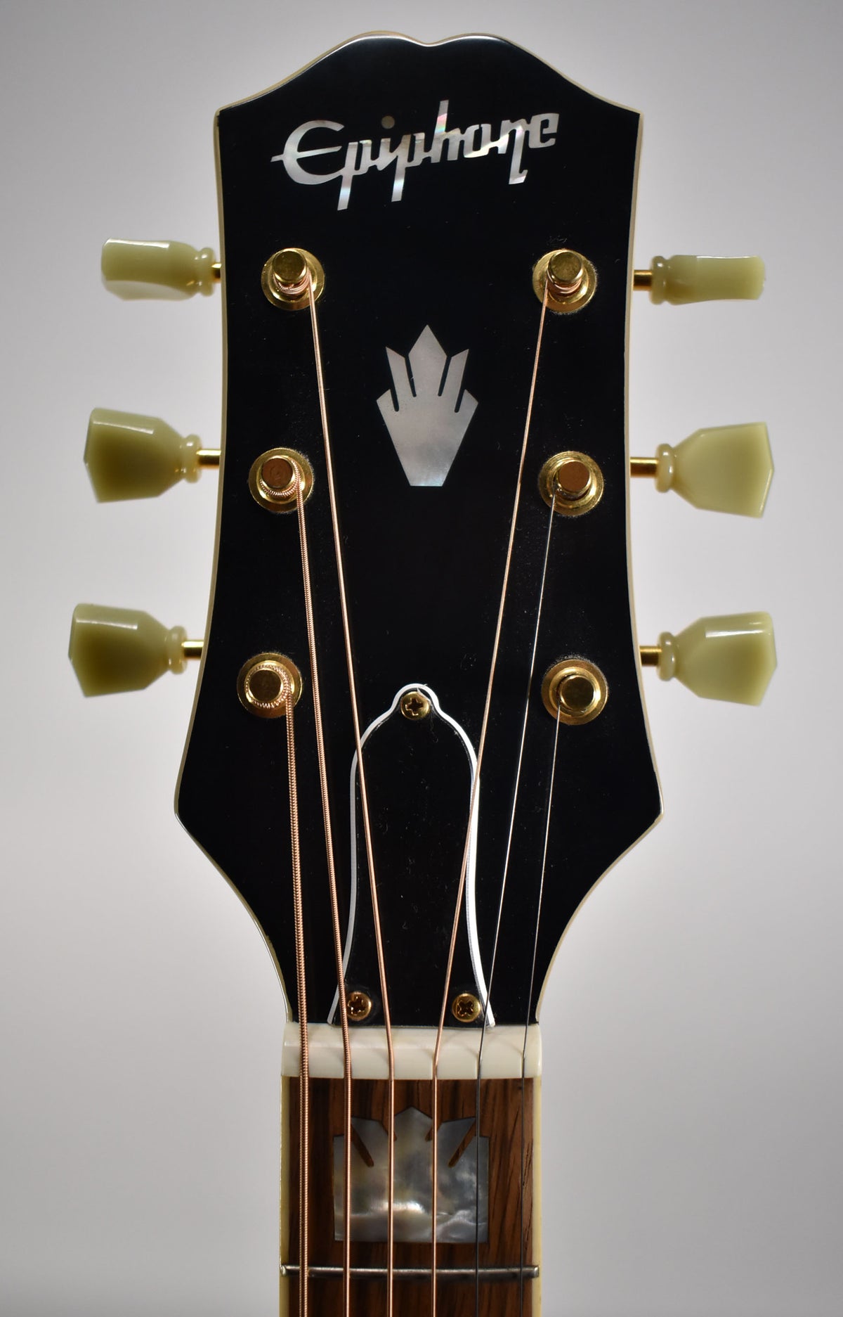 Close-up of the black gloss headstock with mother-of-pearl inlay, gold tuners with aged green buttons, and the top of the fretboard.