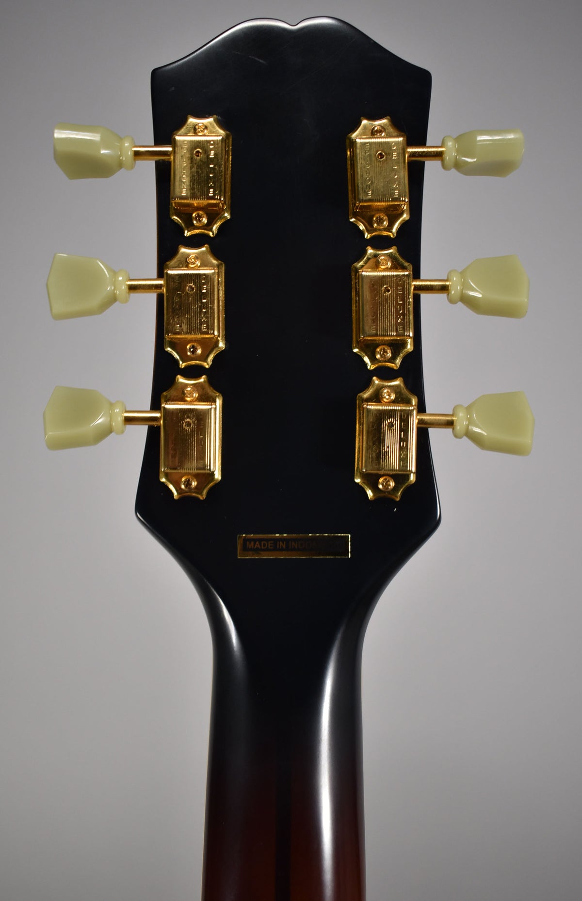 The back of the guitar's headstock and upper neck, showing six gold tuners with cream buttons on a glossy black finish.