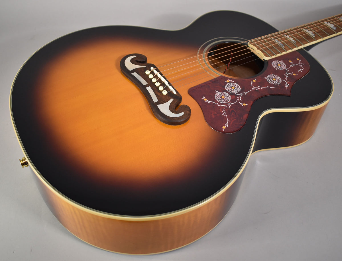 Upper body of a J-200 acoustic guitar in aged vintage sunburst gloss, showing the ornate pickguard and bridge.