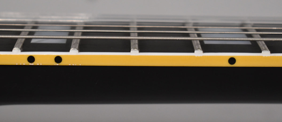 Close-up of the ebony fretboard with trapezoid inlays, showing the binding with two black side dots and light aging.