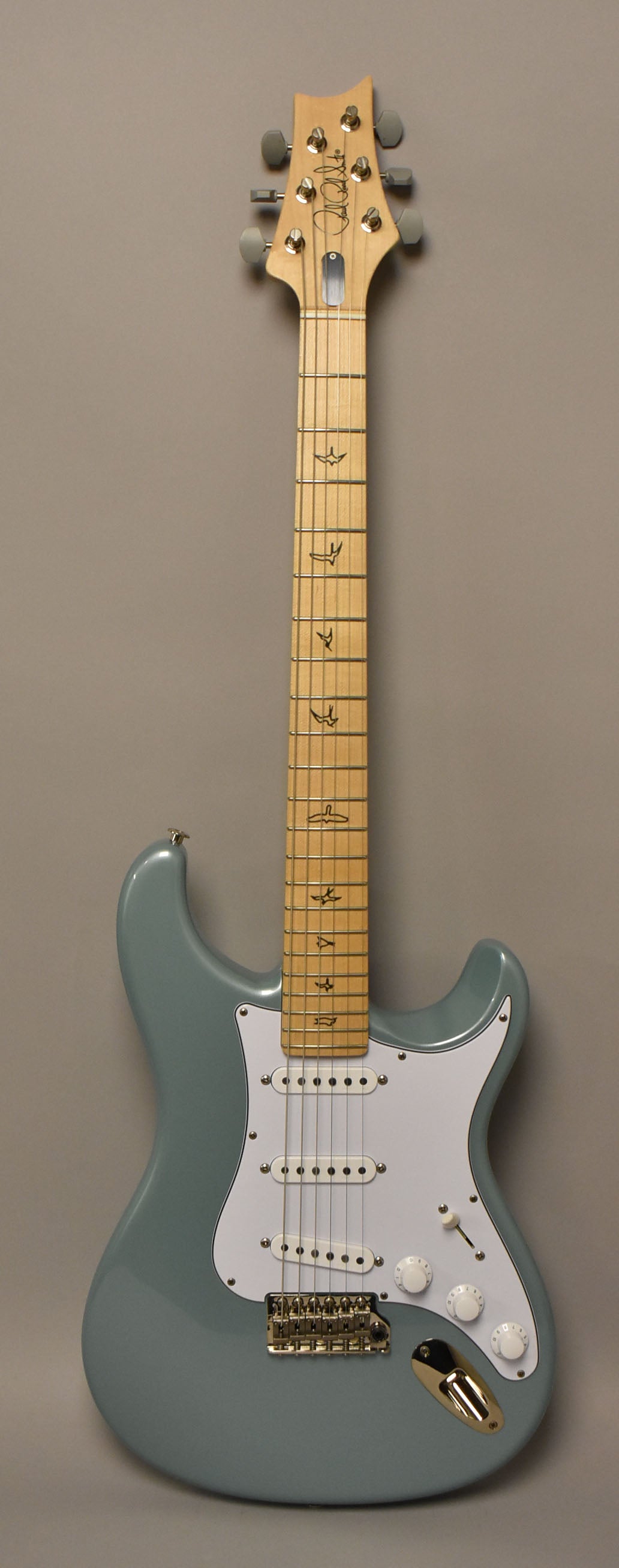 Full front view of a light blue electric guitar with a maple neck, white pickguard, three single-coil pickups, and gold hardware.