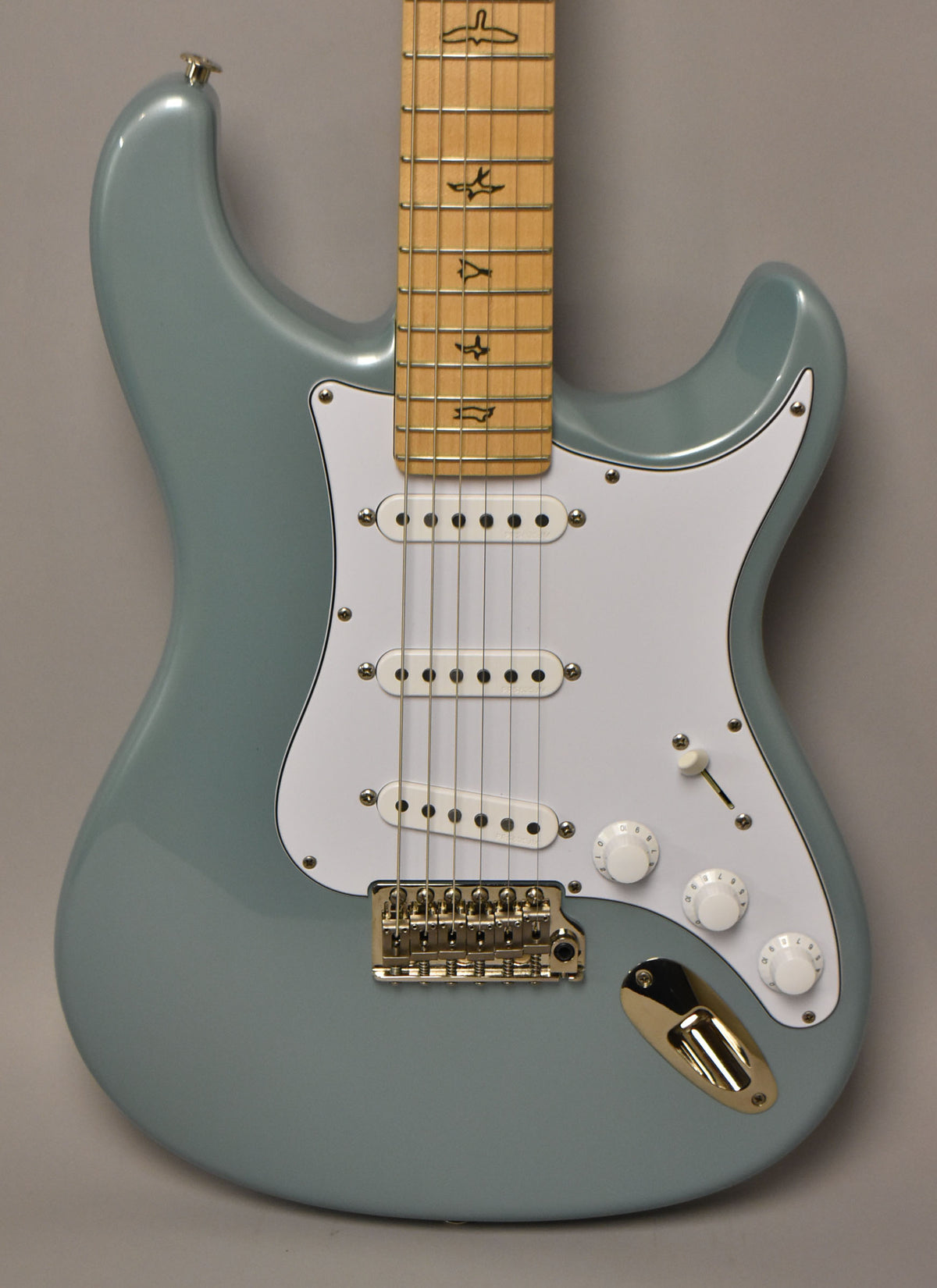 Full front view of a light blue electric guitar with a white pickguard, three white single-coil pickups, and gold hardware.