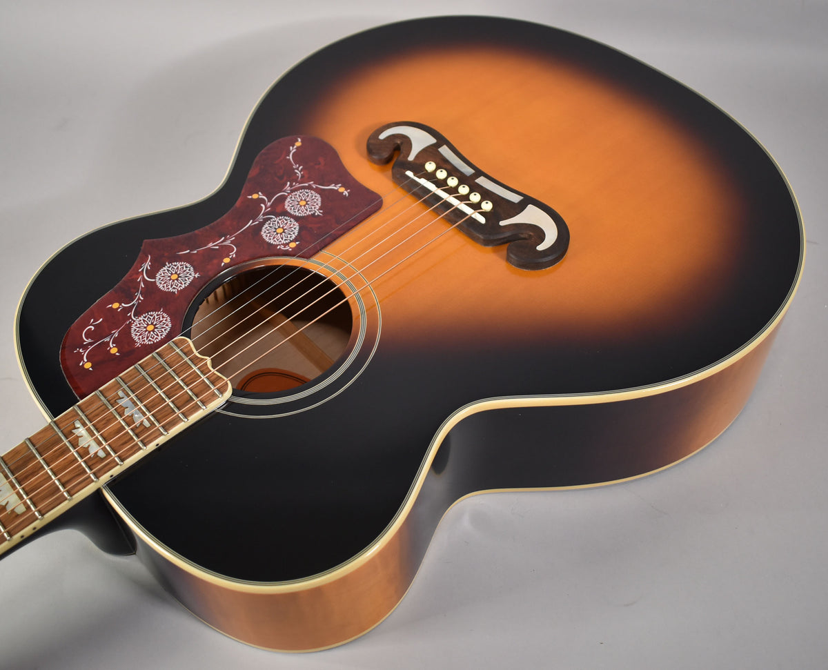 The J-200's aged vintage sunburst gloss body is angled, showing its ornate pickguard, bridge, and neck with block inlays.