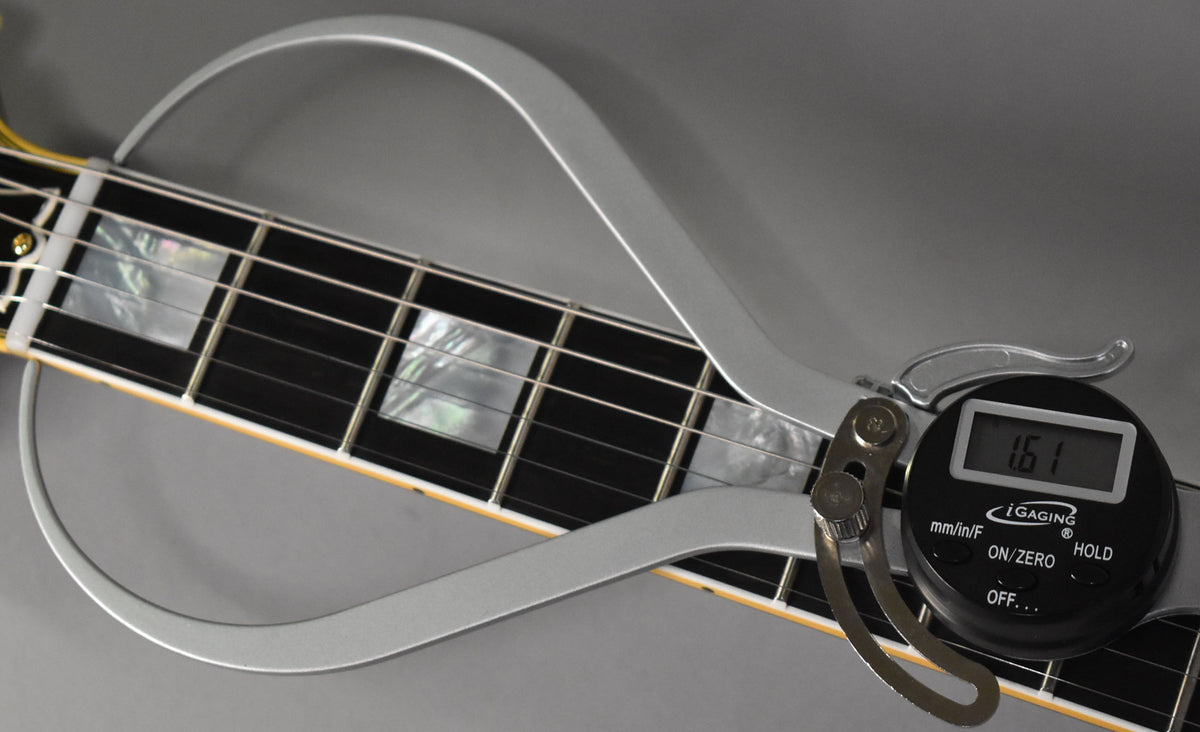 A digital string action gauge shows 1.61mm over the guitar's ebony fretboard with mother-of-pearl block inlays.
