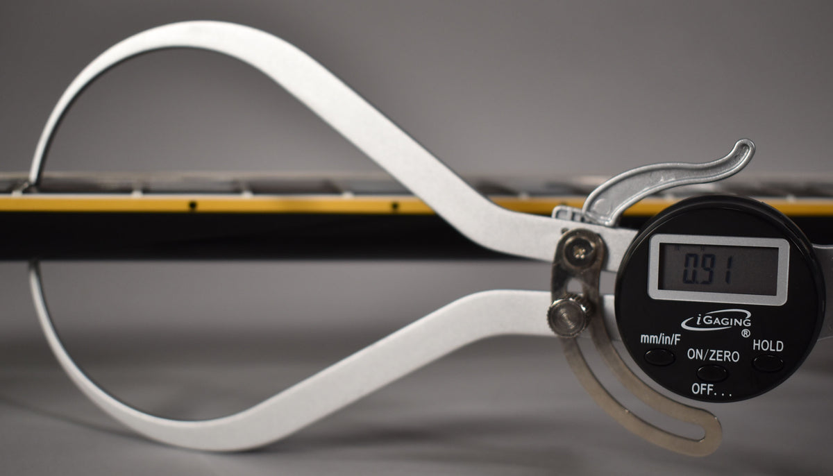 A digital caliper measures the black ebony fretboard and yellow binding of the guitar neck, displaying "0.91".