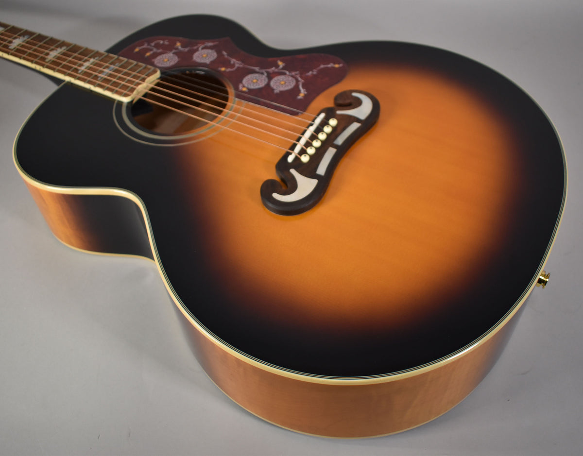 The J-200's sunburst gloss top, with a floral pickguard and ornate bridge, is angled to show the light-colored wood sides.