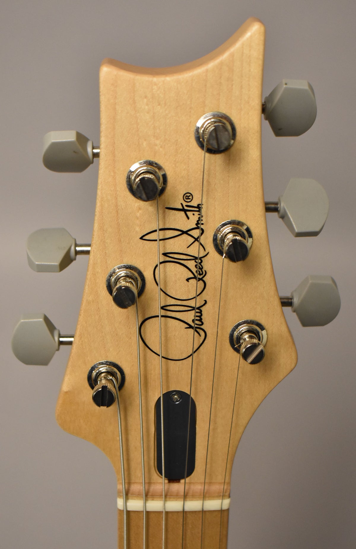 Close-up of the guitar's natural wood headstock, showing six light gray tuning pegs, chrome hardware, and a black truss rod cover.