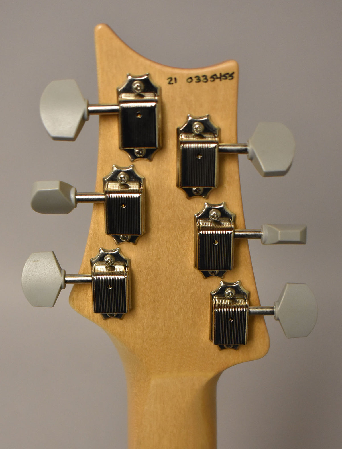 Rear view of the guitar's natural wood headstock and neck, showing six chrome tuners with light gray hexagonal buttons.