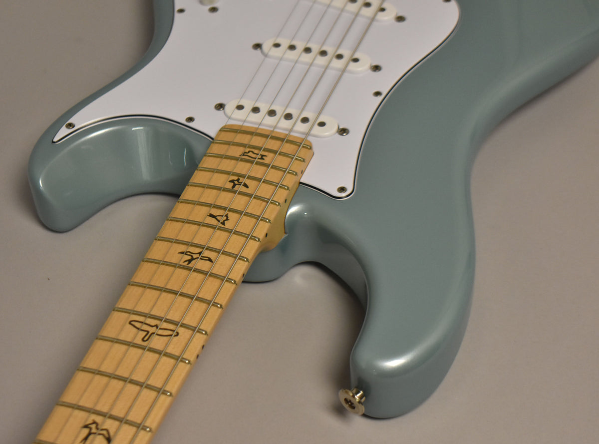 Close-up of the guitar's glossy polar blue body and white pickguard, with the maple fretboard and bird inlays angled across the frame.