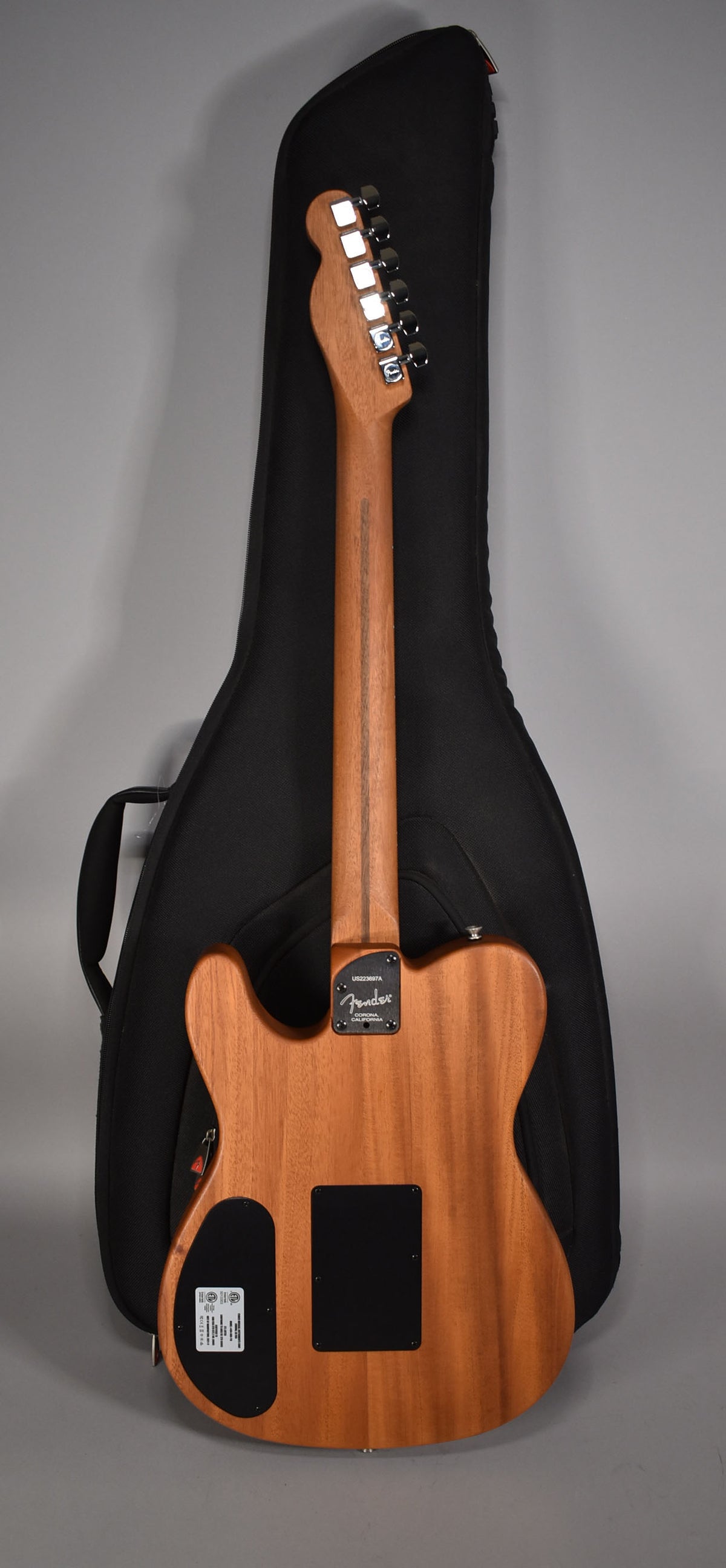 The guitar's back is a natural wood finish, with a black neck plate, two black control covers, and a black gig bag behind it.