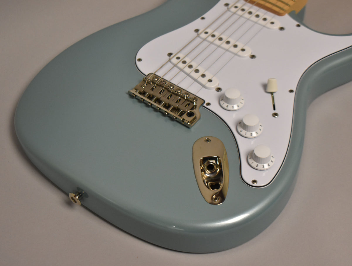 The lower body of a glossy polar blue electric guitar, showing its white pickguard, gold hardware, and three white control knobs.