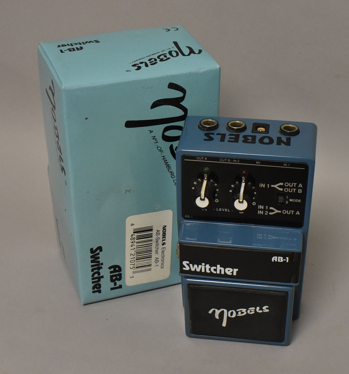 A light blue switcher pedal with black footswitches and two black knobs, shown next to its matching box.