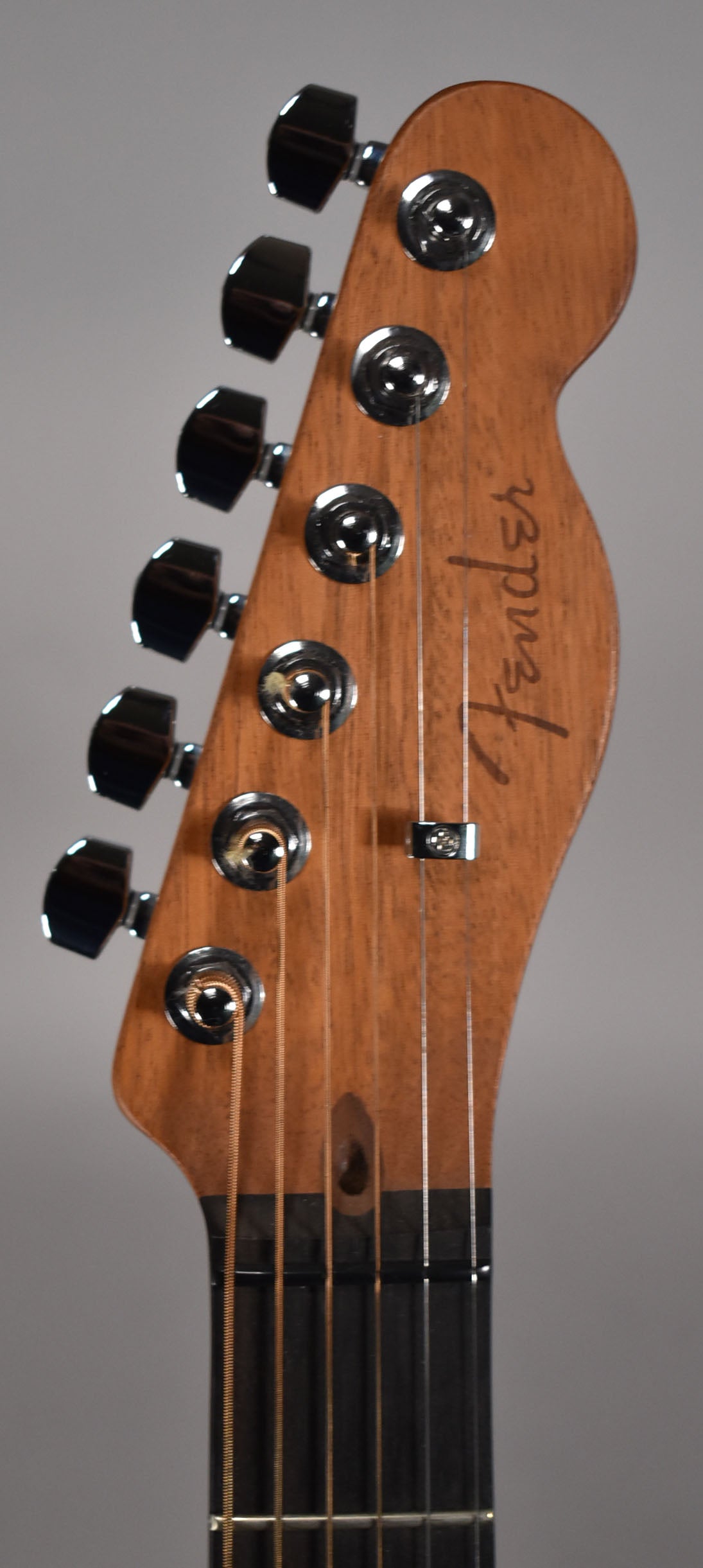Close-up of the guitar's light brown wooden headstock, angled slightly left, with six chrome tuners and a string tree.