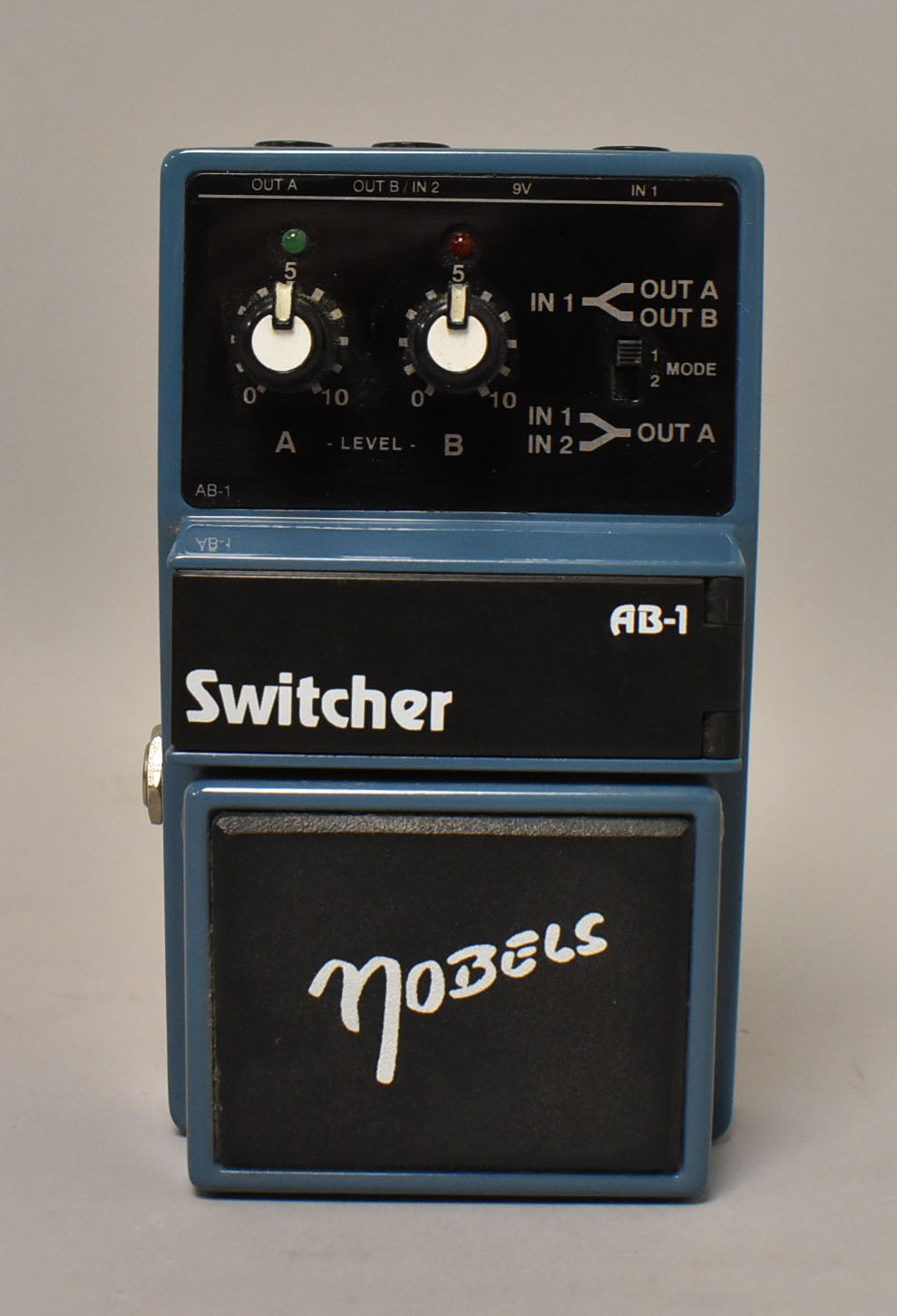 A blue switcher pedal, viewed from the front, with two black level knobs, a mode switch, and a black footswitch.